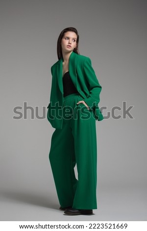 Fashion portrait of a charming girl dressed in a green suit. Gray background. Royalty-Free Stock Photo #2223521669