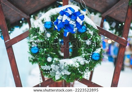 Christmas wreath close-up, outdoors in winter, covered with snow. Green spruce wreath with blue balls and decorations.