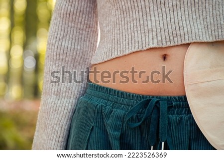 woman abdomen exposing the navel and an ostomy bag in the forest Royalty-Free Stock Photo #2223526369