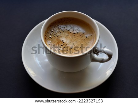 Juicy freshly brewed coffee with foam in a white cup on a black background. Beautiful cup of coffee close-up from above. Black background.