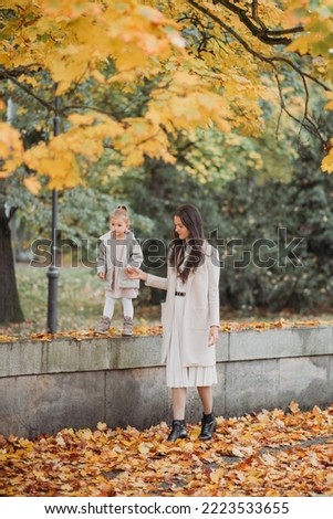 Stylish little girl with mom walks in the park. A beautiful girl with her daughter walks in the autumn park. Happy mother with a child plays in the autumn park. Happy motherhood. High quality photo