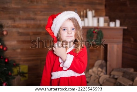 Beautiful little blonde baby girl, has happy fun cheerful smiling face, blue eyes, dressed in red Christmas Santa suit. Kids holiday fashion. Close up. Winter background. Family portrait.