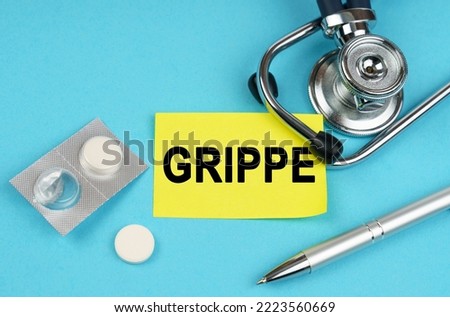 Medical concept. On a blue surface, a stethoscope, pills, a pen and a yellow sticker with the inscription - Grippe Royalty-Free Stock Photo #2223560669