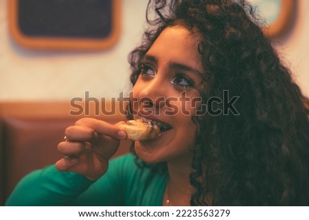 Curly-haired brunette girl enjoys a cup of coffee in a cafe, besides cinnamon rolls