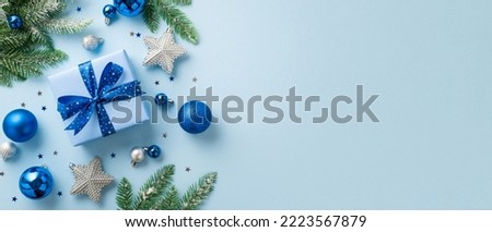 Christmas concept. Top view photo of big present box with ribbon bow blue and white baubles silver star ornaments pine branches in frost and confetti on isolated light blue background with copyspace
