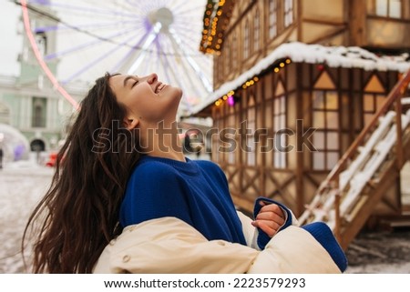 Joyful young caucasian wooman tipped her head laughing with closed eyes outside. Brunette wears sweater and jacket. Positive moments, vacation concept.