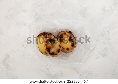 Rotten spoiled potatoes in plastic bag on grey textured background. Concept - Incorrect storage of products. Reduction of organic food waste.