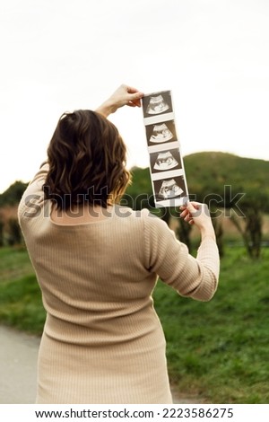 pregnant couple looking at ultrasound picture together. a pregnant couple stands with their backs. future parents