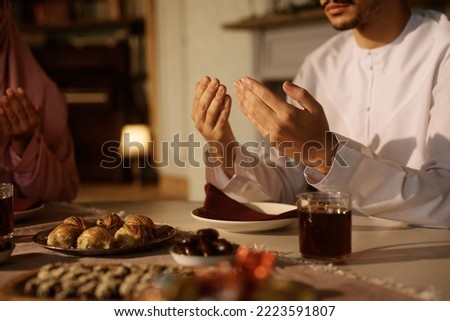 Close up of Middle Eastern man and his wife praying at dining table. Royalty-Free Stock Photo #2223591807