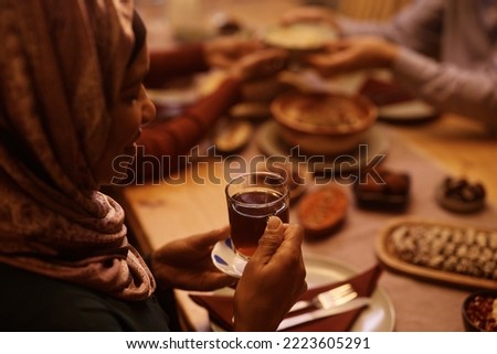 Close up of African American Muslim woman having cup of traditional tea during family meal at dining table. Royalty-Free Stock Photo #2223605291