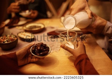 Close up of father pouring milk into daughter's glass during Ramadan meal at dining table. Royalty-Free Stock Photo #2223605325