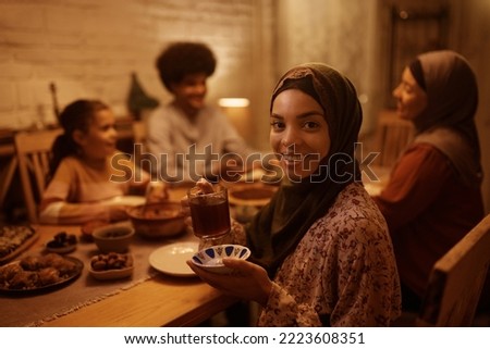 Young Muslim woman having dinner with her extended family and drinking Turkish tea while looking at camera. Royalty-Free Stock Photo #2223608351