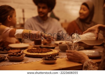 Close up of Middle Eastern woman having meal with her family and pouring milk into a drinking glass at dining table. Royalty-Free Stock Photo #2223608355