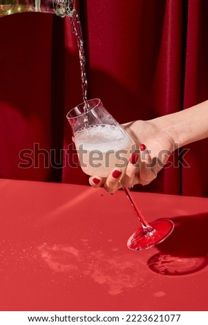 Woman hand holding glass and pouring wine of bottle. Woman tasting white wine on red background. Minimal trendy style composition with person and champagne. Pouring wine and female hand with glass Royalty-Free Stock Photo #2223621077