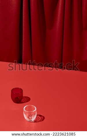 Trendy coloured background with textile. Red background with red table and drapery textile with shadows from glass. Aesthetic red backdrop. Minimal composition with empty place on red background Royalty-Free Stock Photo #2223621085