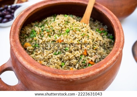 Clay pot with peruvian Arroz con Pollo, which is made of rice, chicken parts, peas, corn, aji hot pepper and cilantro Royalty-Free Stock Photo #2223631043