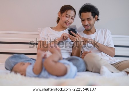 Mom and father use mobile phone enjoy online shopping baby happy laying on bed playing