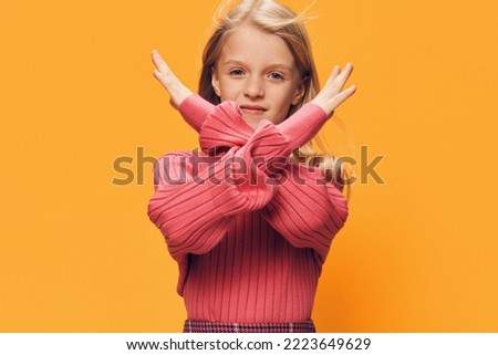 a cute, calm, thoughtful girl stands in pink clothes on a yellow background and crosses her arms as a sign of prohibition, looking at the camera