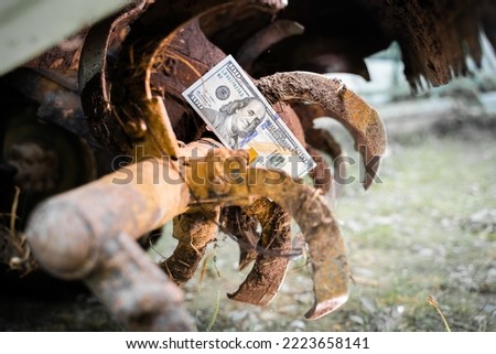 Stopped rural industry due to financial problems. A hundred dollar bill close-up on the teeth of a tractor rototiller. Repair and maintenance of agricultural machinery. Payment for services