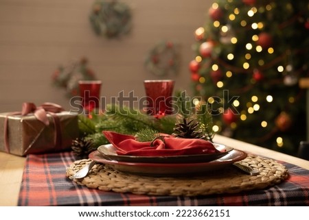 Christmas and New Year 2023, a beautiful setting of the New Year's table in red, against the background of a decorated Christmas tree and a window with a winter landscape Royalty-Free Stock Photo #2223662151
