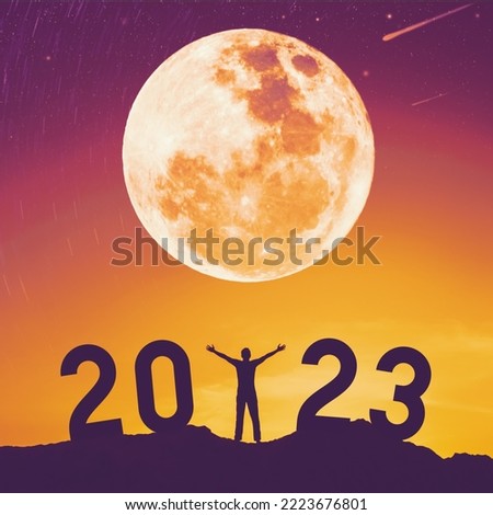 Man raise hand up on sunset sky with full moon at top of mountain and number 2023 abstract background. Happy new year and holiday concept. Vintage tone filter effect color style. Royalty-Free Stock Photo #2223676801