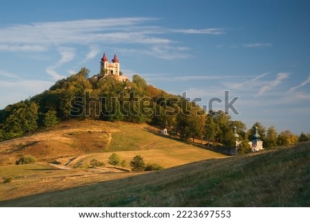 Historical building of church on calvary in Banska Stiavnica, listed in UNESCO world heritage, built on top of hill with meadows and fields with terrain waves on beautiful autumn day Royalty-Free Stock Photo #2223697553