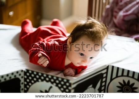 Baby girl on the  bed. Caucasian cute toddler laying on the stomach. Blonde hair 3 month old infant looking at high contrast cards