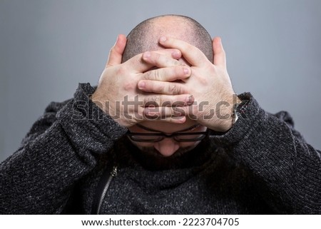 The bald man put his head down and wrapped his arms around it. Despair, stress and pain. Close-up. Grey background. Royalty-Free Stock Photo #2223704705