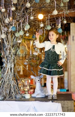 a girl in a holiday dress sitting in a room with Christmas decoration