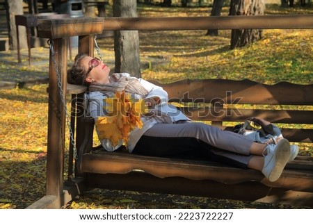 The photo was taken in the Odessa park called Dyukovsky Garden. The picture shows a young pretty woman resting on a bench in an autumn park with a bouquet of yellow leaves.