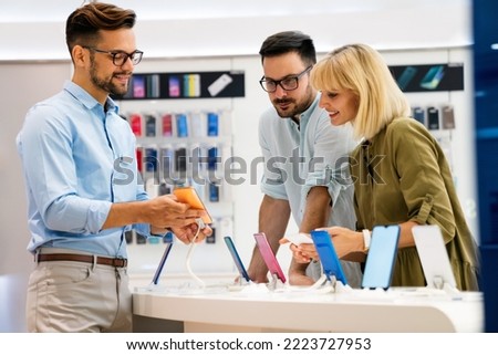 Happy seller man helping to people to buy a new digital smart device in tech store. Royalty-Free Stock Photo #2223727953