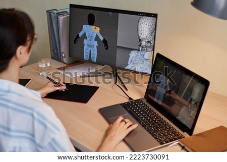 Young female designer building digital 3D models for videogame characters at workplace and using pen tablet Royalty-Free Stock Photo #2223730091