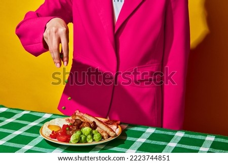 Woman cooking fried eggs, English breakfast on plate on green tablecloth. Delicious food. Vintage, retro style interior. Food pop art photography. Complementary colors. Copy space for ad, text Royalty-Free Stock Photo #2223744851
