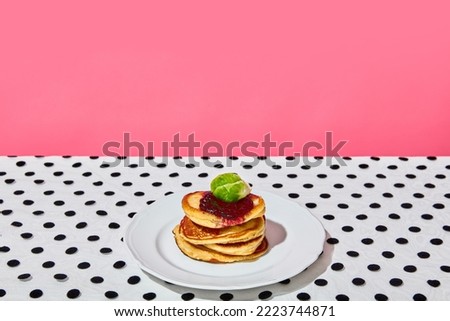 Plate of delicious sweet pancakes with jam on dotted white tablecloth over pink background. Vintage, retro style interior. Food pop art photography. Complementary colors. Copy space for ad, text
