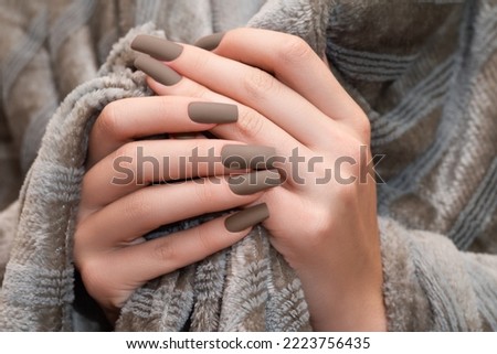 Female hands with brown nail design. Mate brown nail polish manicure. Female model hands with perfect brown manicure on beige fluffy fabric. Royalty-Free Stock Photo #2223756435