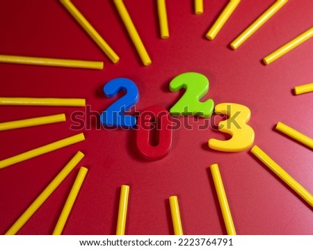New Year's numbers on the table 2023 and decorative colorful sticks on a red background.
