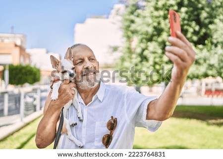 Senior man smihugging chihuahua making selfie by the smartphone at park