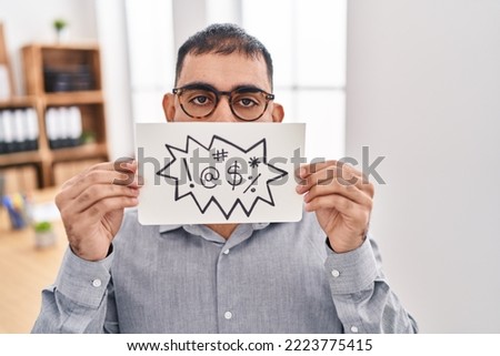 Middle east man with beard holding banner with swear words sticking tongue out happy with funny expression.  Royalty-Free Stock Photo #2223775415