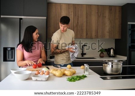 Two young latin people talking about a recipe while cooking together at kitchen. Royalty-Free Stock Photo #2223785349