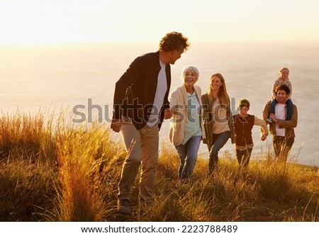 Follow the leader. A multi-generational family walking up a grassy hill together at sunset with the ocean in the background. Royalty-Free Stock Photo #2223788489