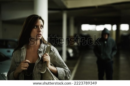 I think that guy is following me.... A young woman in a parking lot looking concerned as someone follows her. Royalty-Free Stock Photo #2223789349