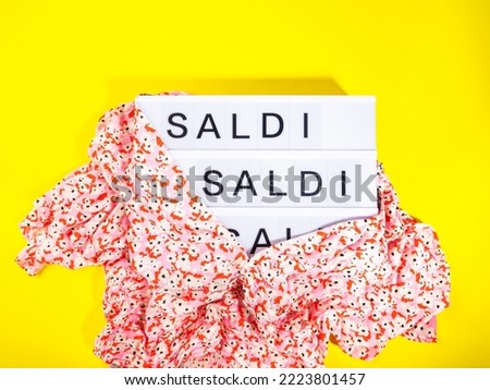 Sale in Italian text on lightbox, fashion discount promotion in women clothing store concept with floral red blouse on bold yellow background. Trendy flat lay with hard shadows