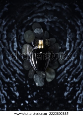 Black perfume bottle on stones in water. Glass container for cosmetics with waves on the water. Royalty-Free Stock Photo #2223803885