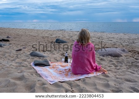 One woman on the seashore. Sitting covered with a towel and sipping champagne.