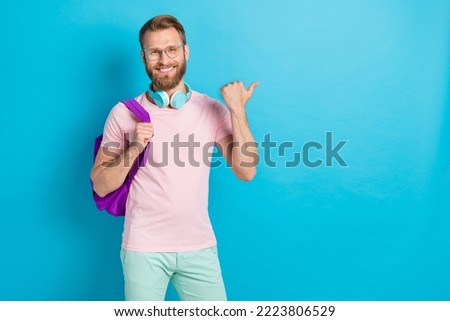 Photo portrait of attractive young man hipster headphones point empty space wear trendy pink clothes isolated on cyan color background