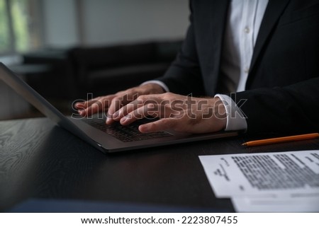 Businessman in formal suit typing on laptop near contract at office workplace. Concept of important working moments, document signing, working process, important notes, promotion, ceo