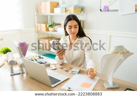 Successful young woman counting money and doing finances while working selling jewelry online Royalty-Free Stock Photo #2223808883