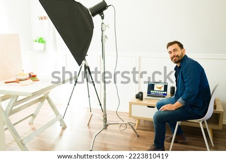 Caucasian smiling photographer doing photo editing at the laptop after a professional shooting at the studio