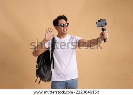 Young Asian tourist backpacker man smiling and taking a selfie and blog isolated on beige background Royalty-Free Stock Photo #2223840153