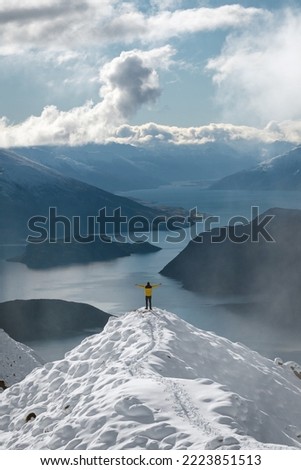 Man with open arms at peak of snowy mountain with amazing panoramic view of lakes and mountain range in winter. Roy's Peak iconic lookout. Wanaka, New Zealand. Vertical photography